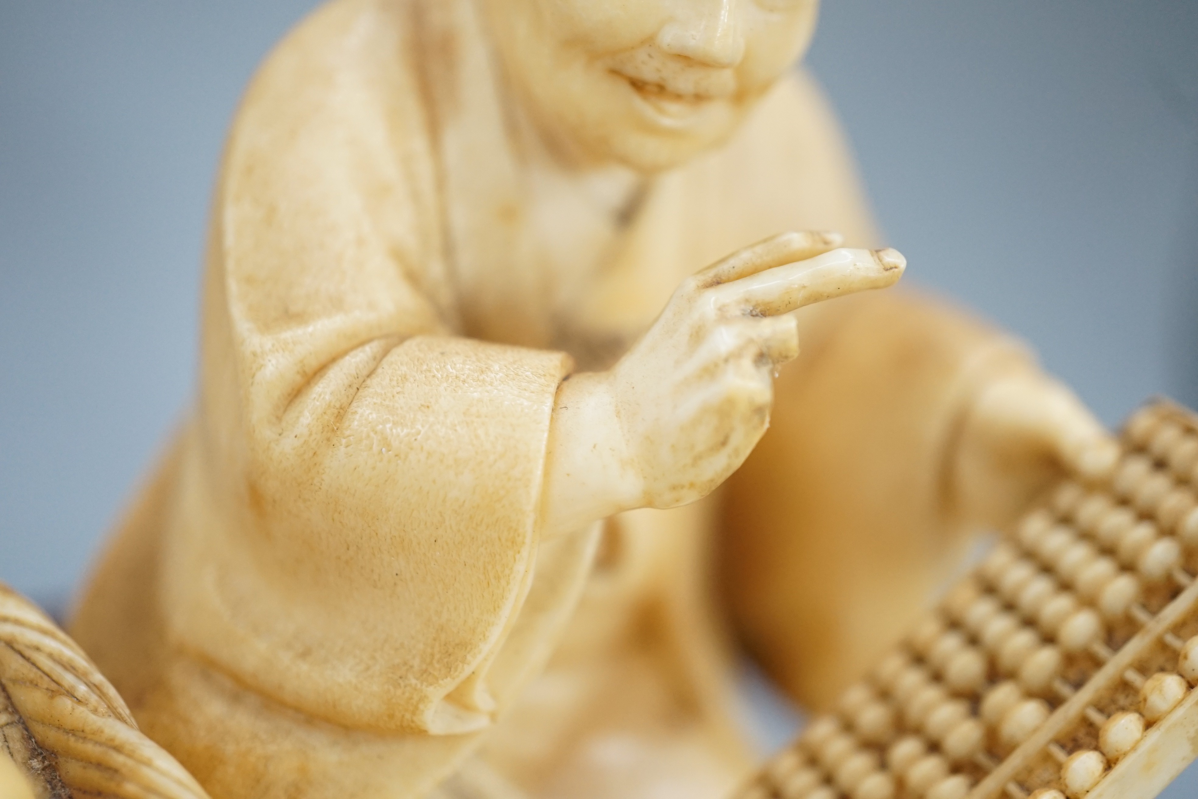 A Japanese ivory okimono of a street vendor kneeling and holding an abacus, Meiji period, 8cm, associated wood stand